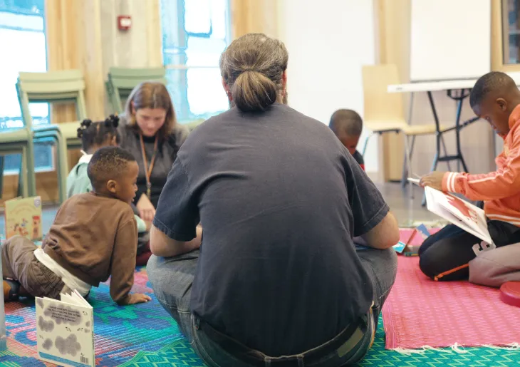 Un groupe d’enfants participe à un atelier de lecture avec 2 travailleurs sociaux à la Maison des réfugié·es.