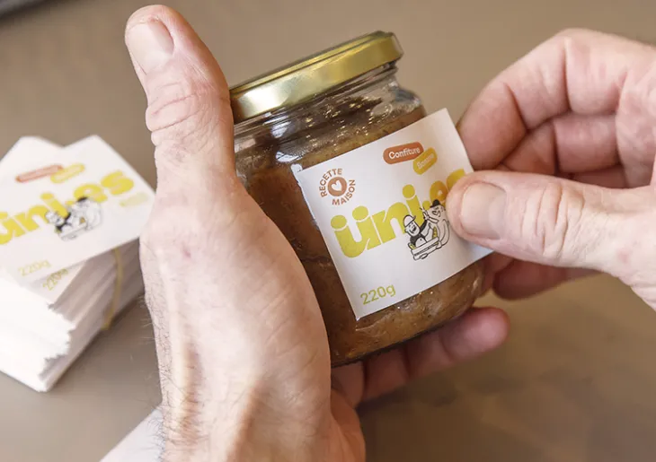 Gros plan sur une main en train de coller une étiquette sur un pot de confiture