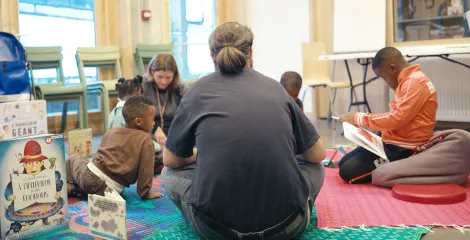 Un groupe d’enfants participe à un atelier de lecture avec 2 travailleurs sociaux à la Maison des réfugié·es.