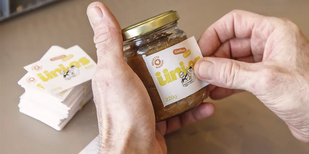 Gros plan sur une main en train de coller une étiquette sur un pot de confiture